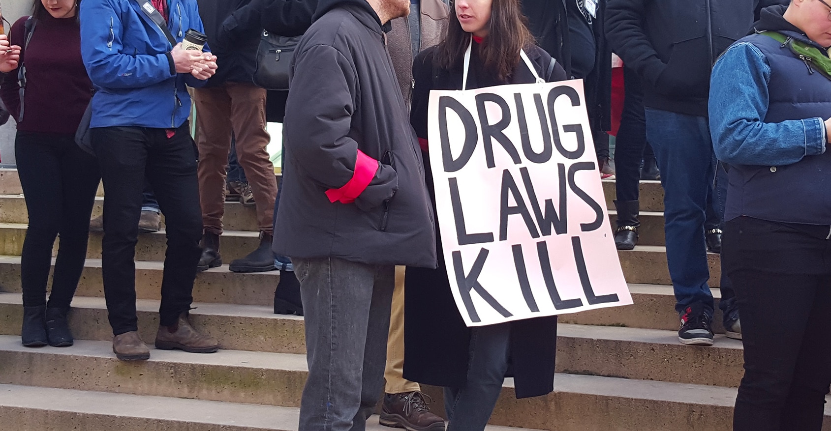 Sign reading "drug laws kill" over the neck of a protester